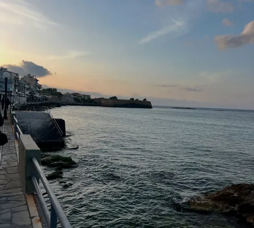 Ο παραλιακός πεζόδρομος του Κουμ Καπί και η θάλασσα στο σούρουπο, με τα βράχια στο βάθος.