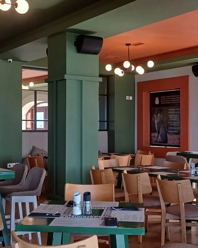 Η αίθουσα μέσα: πράσινες κολόνες, ξύλινες καρέκλες και στρωμένα τραπέζια.